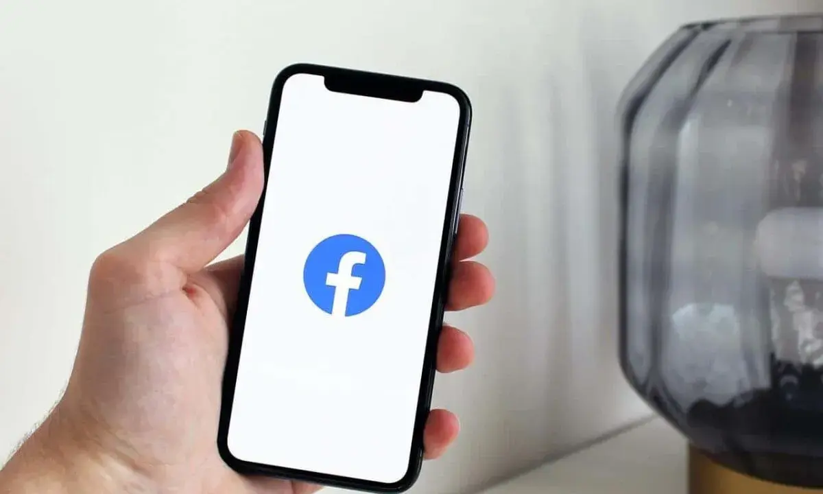 Dłoń trzyma smartfon z widocznym logo na FB.