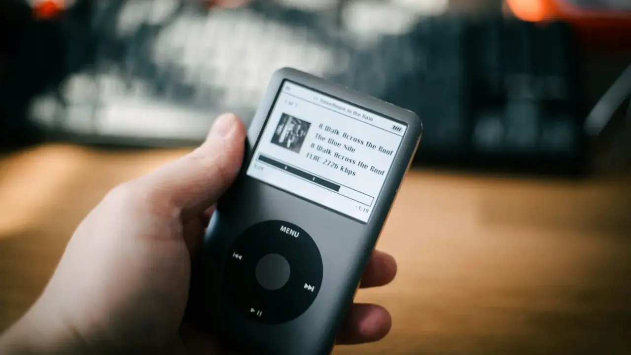 Dłoń trzyma iPoda z listą utworów, w tym "A Walk Across the Roof". Idealny do słuchania muzyki, jakbyś używał audiograbber po polsku.