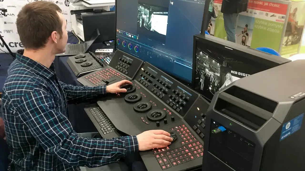 Mężczyzna pracuje przy konsoli do obróbki filmu, dostosowując kolory na dużym monitorze.