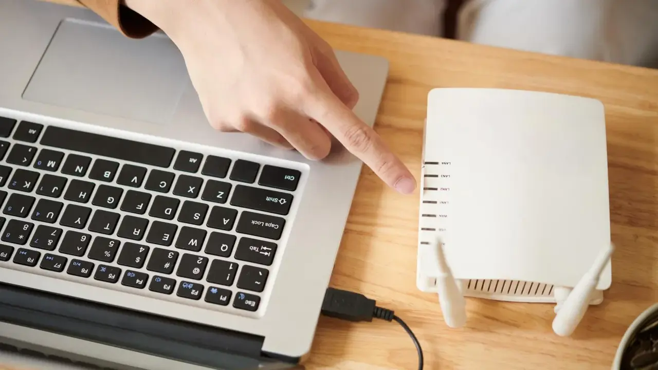 Ręka wskazuje na router, podłączony do laptopa. To pierwszy krok, by skonfigurować drukarkę HP.