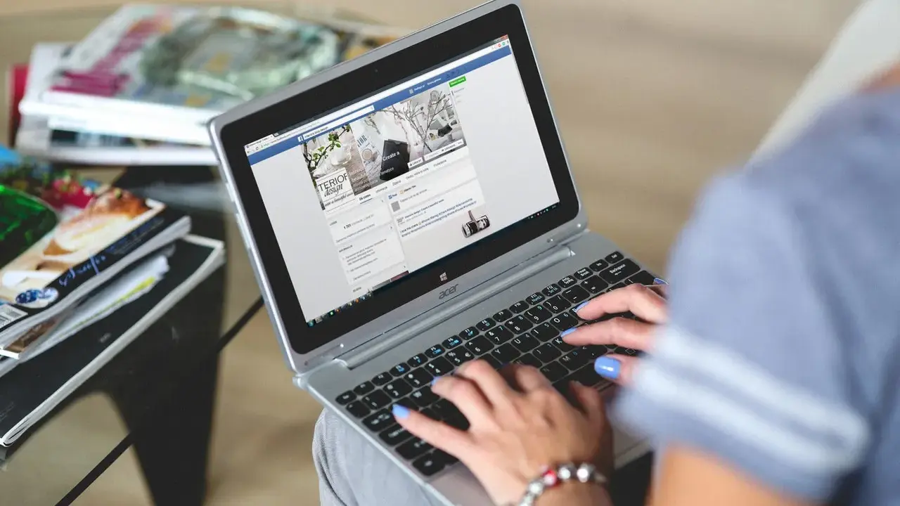 Kobieta pisze na laptopie, przeglądając co to jest post na Facebooku. Obok leżą czasopisma.