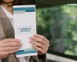 Osoba prezentuje ulotkę z programem konferencji. Dowiedz się, jak zrobić ulotkę, która przyciągnie uwagę.
