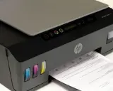 Drukarka HP Smart Tank 515, widoczne kolorowe zbiorniki z tuszem i wychodzący papier. Czas na czyszczenie głowicy, by wydruki były idealne.