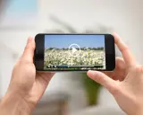Dłonie trzymają smartfon z widokiem na pole stokrotek. Na ekranie odtwarzacz wideo, idealny do edycji i przycinania filmów.