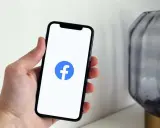 Dłoń trzyma smartfon z widocznym logo na FB.