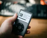 Dłoń trzyma iPoda z listą utworów, w tym "A Walk Across the Roof". Idealny do słuchania muzyki, jakbyś używał audiograbber po polsku.