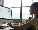 Kobieta pracuje przy komputerze, na ekranie widoczny jest tekst "Identify your topic". Może szukać informacji, jak wstawić tło w Wordzie.