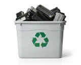 Pojemnik z zielonym symbolem recyklingu wypełniony po brzegi zużytymi tonerami.