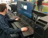 Mężczyzna pracuje przy konsoli do obróbki filmu, dostosowując kolory na dużym monitorze.