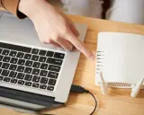 Ręka wskazuje na router, podłączony do laptopa. To pierwszy krok, by skonfigurować drukarkę HP.