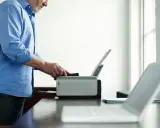 Mężczyzna ustawia drukarkę jako domyślną, przygotowując się do drukowania dokumentów z laptopa.