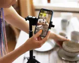 Kobieta z kolorowymi warkoczami ustawia telefon na statywie, by nagrać filmik: jak zrobić rolkę na Instagramie ze zdjęć.