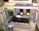 Wnętrze drukarki po otwarciu klapy, widoczne wkłady z tonerem i mechanizmy. Trwa test drukarki.