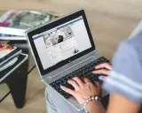 Kobieta pisze na laptopie, przeglądając co to jest post na Facebooku. Obok leżą czasopisma.