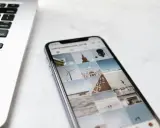 Telefon z Instagramem obok laptopa. Na ekranie telefonu widać siatkę zdjęć, gdzie są aktualności na Instagramie, m.in. wiatrak i budynek.