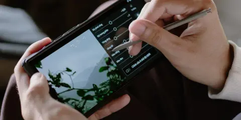 Ręce trzymają smartfon, na którym edytowany jest film. Stylus dostosowuje parametry, by pokazać, jak zrobić film na TikToku.
