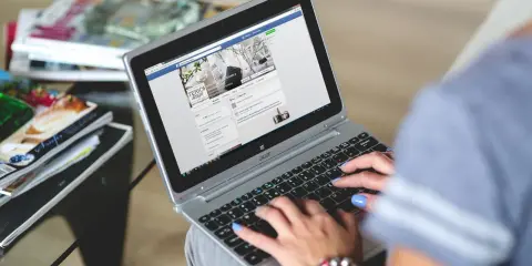 Kobieta pisze na laptopie, przeglądając co to jest post na Facebooku. Obok leżą czasopisma.