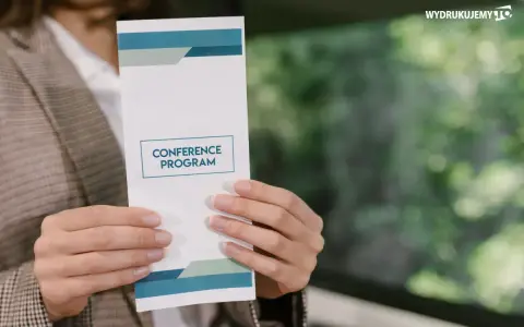 Osoba prezentuje ulotkę z programem konferencji. Dowiedz się, jak zrobić ulotkę, która przyciągnie uwagę.