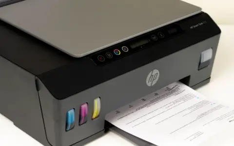 Drukarka HP Smart Tank 515, widoczne kolorowe zbiorniki z tuszem i wychodzący papier. Czas na czyszczenie głowicy, by wydruki były idealne.