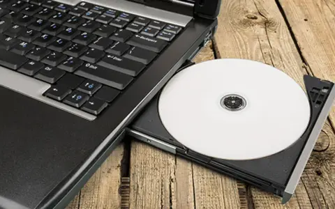 Laptop z wysuniętym napędem CD, na którym leży biała płyta. Idealne do nagrywania z cdburnerxp portable.