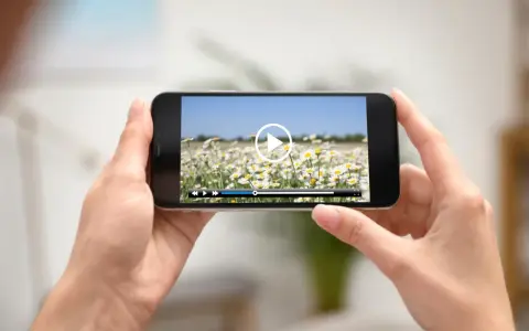 Dłonie trzymają smartfon z widokiem na pole stokrotek. Na ekranie odtwarzacz wideo, idealny do edycji i przycinania filmów.