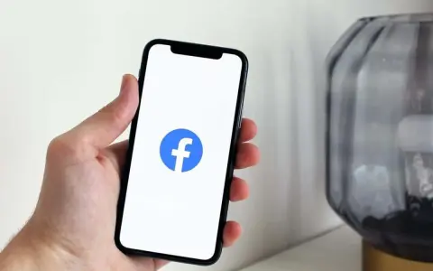 Dłoń trzyma smartfon z widocznym logo na FB.