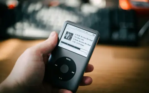 Dłoń trzyma iPoda z listą utworów, w tym "A Walk Across the Roof". Idealny do słuchania muzyki, jakbyś używał audiograbber po polsku.