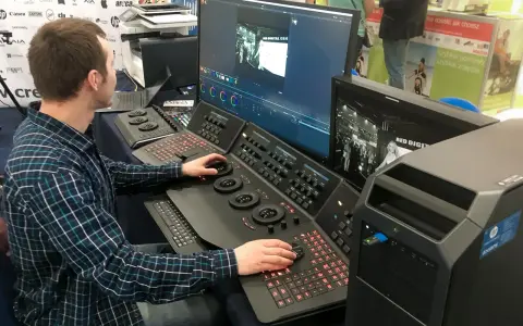 Mężczyzna pracuje przy konsoli do obróbki filmu, dostosowując kolory na dużym monitorze.