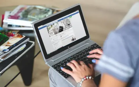 Kobieta pisze na laptopie, przeglądając co to jest post na Facebooku. Obok leżą czasopisma.