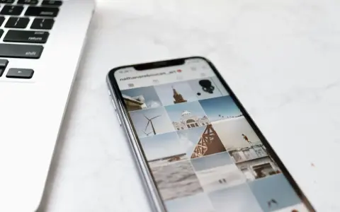 Telefon z Instagramem obok laptopa. Na ekranie telefonu widać siatkę zdjęć, gdzie są aktualności na Instagramie, m.in. wiatrak i budynek.