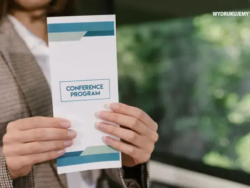 Osoba prezentuje ulotkę z programem konferencji. Dowiedz się, jak zrobić ulotkę, która przyciągnie uwagę.