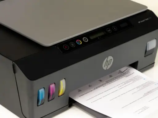 Drukarka HP Smart Tank 515, widoczne kolorowe zbiorniki z tuszem i wychodzący papier. Czas na czyszczenie głowicy, by wydruki były idealne.