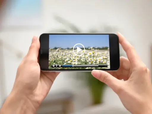 Dłonie trzymają smartfon z widokiem na pole stokrotek. Na ekranie odtwarzacz wideo, idealny do edycji i przycinania filmów.