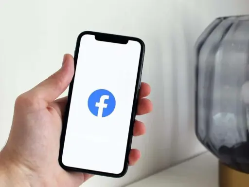 Dłoń trzyma smartfon z widocznym logo na FB.