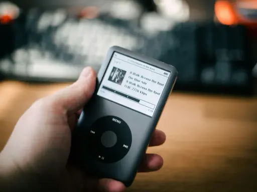 Dłoń trzyma iPoda z listą utworów, w tym "A Walk Across the Roof". Idealny do słuchania muzyki, jakbyś używał audiograbber po polsku.