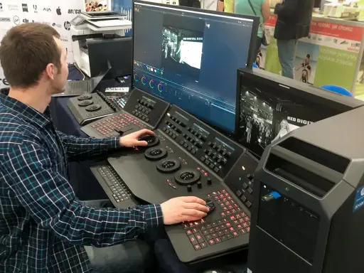 Mężczyzna pracuje przy konsoli do obróbki filmu, dostosowując kolory na dużym monitorze.