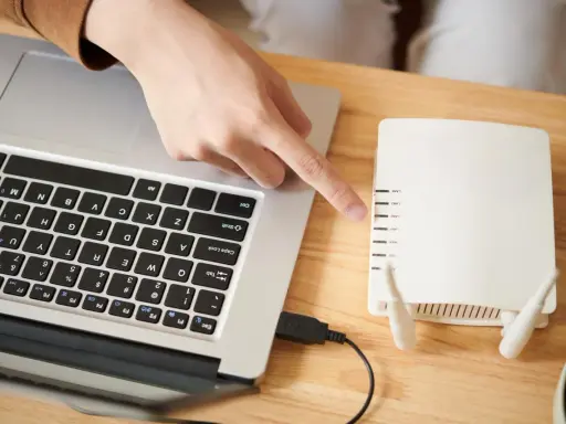 Ręka wskazuje na router, podłączony do laptopa. To pierwszy krok, by skonfigurować drukarkę HP.