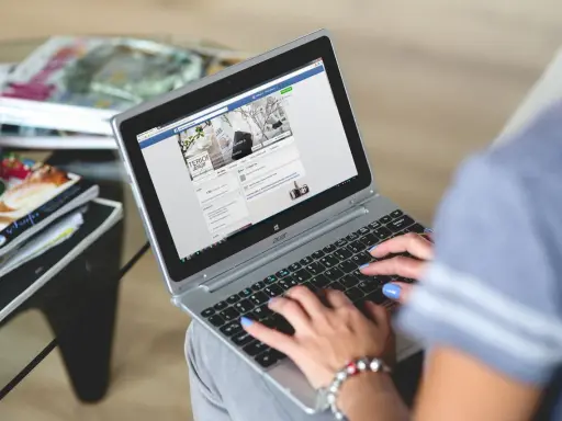 Kobieta pisze na laptopie, przeglądając co to jest post na Facebooku. Obok leżą czasopisma.