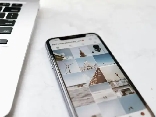 Telefon z Instagramem obok laptopa. Na ekranie telefonu widać siatkę zdjęć, gdzie są aktualności na Instagramie, m.in. wiatrak i budynek.