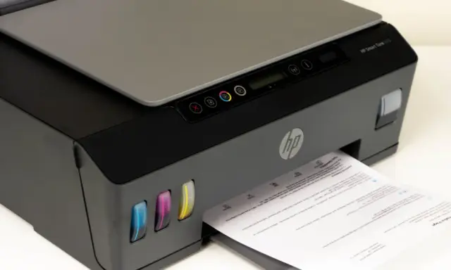 Drukarka HP Smart Tank 515, widoczne kolorowe zbiorniki z tuszem i wychodzący papier. Czas na czyszczenie głowicy, by wydruki były idealne.