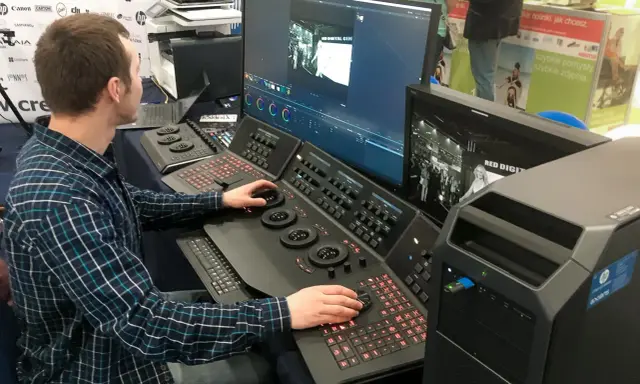 Mężczyzna pracuje przy konsoli do obróbki filmu, dostosowując kolory na dużym monitorze.