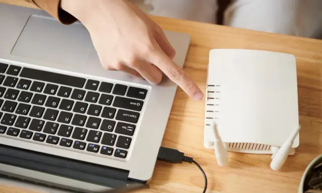 Ręka wskazuje na router, podłączony do laptopa. To pierwszy krok, by skonfigurować drukarkę HP.