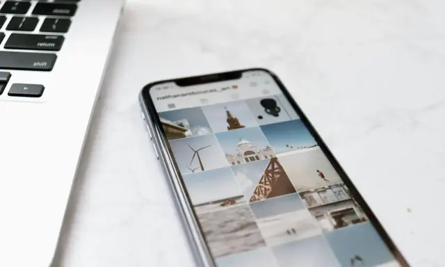 Telefon z Instagramem obok laptopa. Na ekranie telefonu widać siatkę zdjęć, gdzie są aktualności na Instagramie, m.in. wiatrak i budynek.