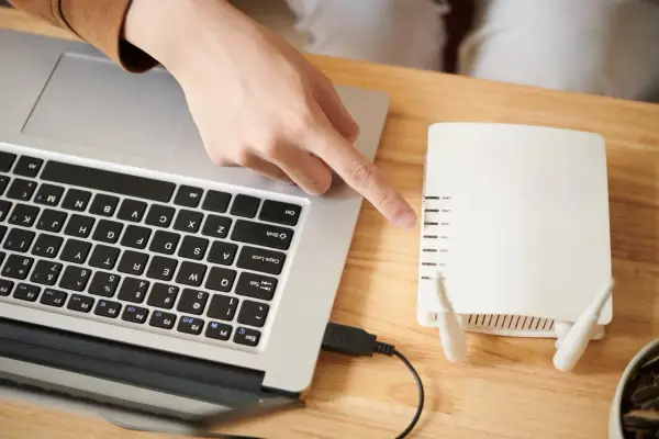 Ręka wskazuje na router, podłączony do laptopa. To pierwszy krok, by skonfigurować drukarkę HP.